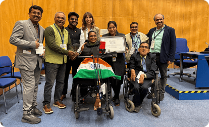 Indian award winner in a wheelchair proudly holding a certificate with the Indian flag, surrounded by a diverse group at an international event celebrating achievement and inclusion.