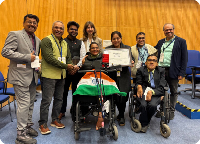 Indian award winner in a wheelchair proudly holding a certificate with the Indian flag, surrounded by a diverse group at an international event celebrating achievement and inclusion.