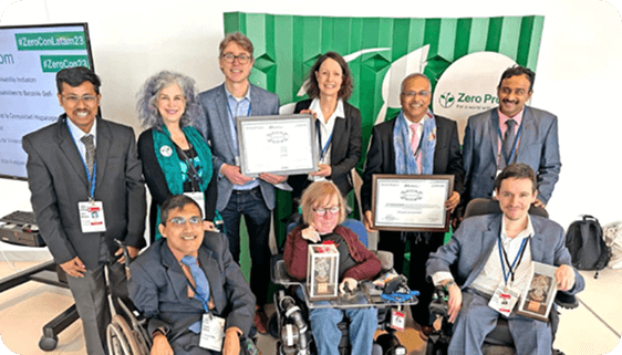 A group of smiling individuals posing with certificates and awards in front of a “Zero Project” backdrop at a formal recognition event.
