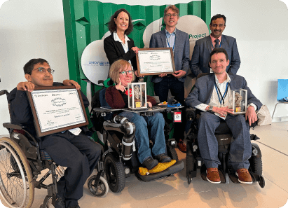 Group of award recipients, including individuals in wheelchairs, proudly holding certificates and trophies at the Zero Project event.